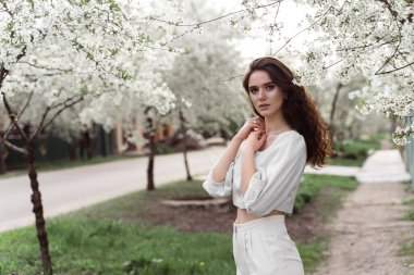 Bahar yaşam tarzı. Beyaz ağaçların yanında, kırsal alanda maskesiz poz veren bir model. Kıvırcık saçlı rüya kızı.