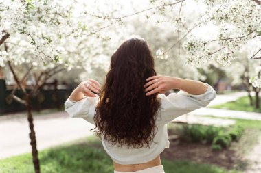 Parkta çiçek açan ağaçların yanında güzel bir kız. Güneşli bir günde dışarıda yürüyüş. Genç bir kadının yaşam tarzı..