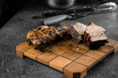 Izgara kaburga, gri arka planda ahşap bir tabakta dilimleniyor. Barbekü dekorasyonu