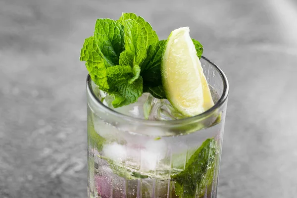 Cocktail with tonic, currant syrup, lime, mint, ice in tall glass on gray background. Puff cold drink with blueberries