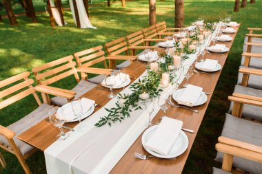 Ormanda köy dekorasyonu olan bir düğün masası. Tabaklar ve masada mumlar olan yeşil bir dal. Yeşil dekorasyon.