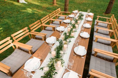 Ormanda köy dekorasyonu olan bir düğün masası. Tabaklar ve masada mumlar olan yeşil bir dal. Yeşil dekorasyon.