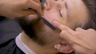 Berber dükkanında ustura kesim adam sakalı. Berber adam yakışıklı bir adam için saç stili yapıyor. 4k video