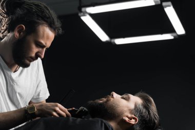 Yakışıklı sakallı adamın berber dükkanında saçı ve sakalı var. Dreadlock berberi müşterinin saçını kesiyor..