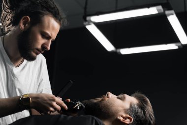 Yakışıklı sakallı adamın berber dükkanında saçı ve sakalı var. Dreadlock berberi müşterinin saçını kesiyor..