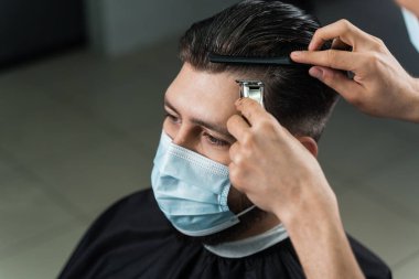 Tıbbi maskeli berber Coronavirus covid-19 karantinasındaki berber dükkanında yakışıklı sakallı müşterilere saç stili yapıyor.