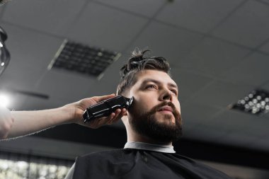 Berber dükkanındaki yakışıklı sakallı adam için düşük soluk makineli saç kesimi. Saçları pürüzsüz kesilmiş.