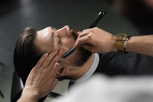 Straight razor cut mans beard in barbershop. Barber man making hairstyle for handsome man
