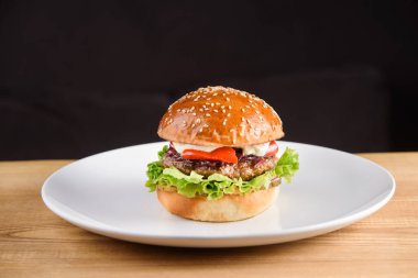 Pirzola, sos, domates, marul, siyah arka planda beyaz tabakta susam..