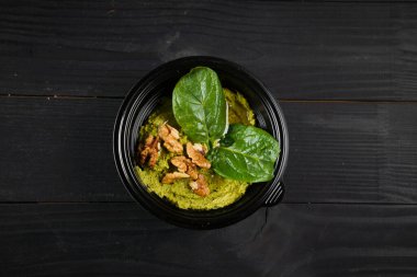 Fesleğenli ve cevizli humus siyah kasede siyah ahşap masada otlarla süslenmiş.