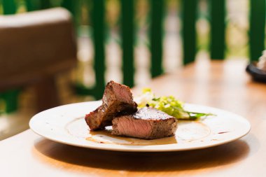 Restoranın arka planında beyaz tabakta biftek. Orta pişmiş sulu et.
