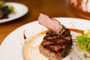 Tahta masada beyaz tabakta biftek. Orta pişmiş sulu et.