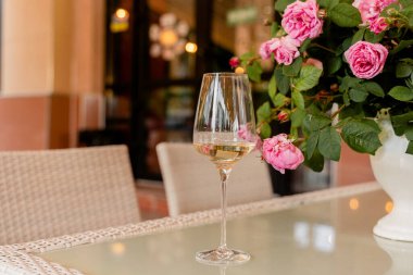 Bir bardak beyaz şarap arka plandaki güllere karşı beyaz vazoda aydınlık masada..