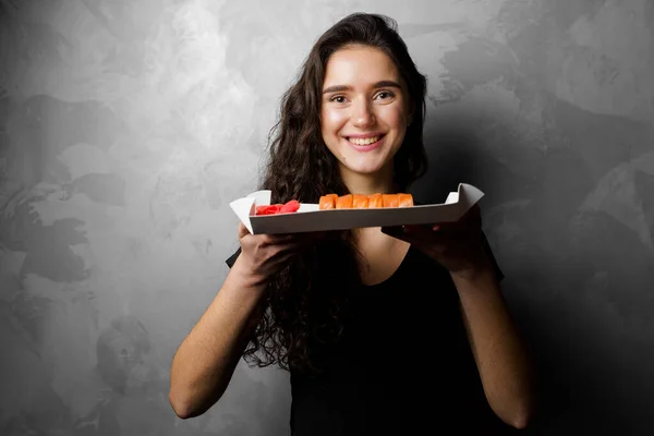 Chica Sosteniendo Rollos Filadelfia Una Caja Papel Sobre Fondo Gris — Foto de Stock