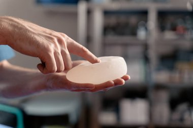 Cerrah kalite kontrolü için silikon implantlarına dokunur ve sıkar. Göğüs büyütme ve kaldırma ameliyatı.