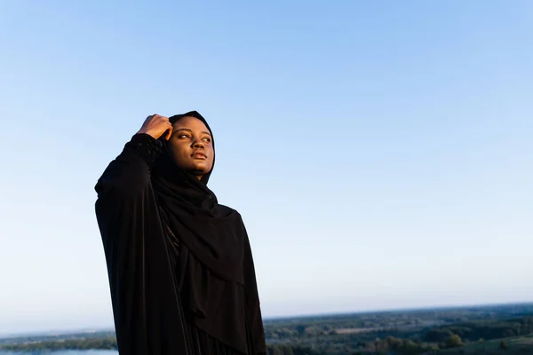 Black muslim woman weared in black robe on blue background. Islamic religion. Celebrating ramadan.
