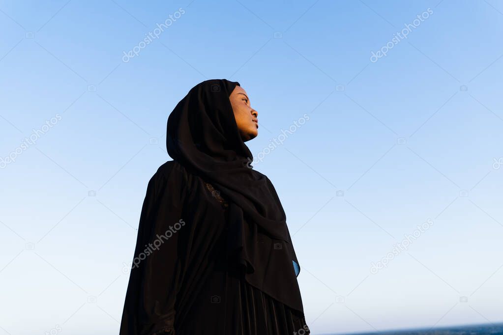 Black muslim woman weared in black robe on blue background. Islamic religion. Celebrating ramadan