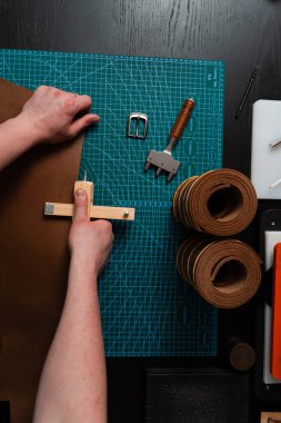 El yapımı deri kemer hazırlığı, hasırın üzerinde tahta kayış kesici var. Esnaf deri şeridi ahşap aletle kesiyor. Zanaatkar, hasırın üzerine tahta kesici kullanarak deri kayış hazırlıyor.