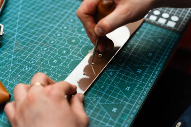 Deri kemer deliklerini yumruklamak ve detaylandırmak. Zanaatkar yeşil bir hasırın el yapımı kemeri için deri kayışlara delikler açıyor. Deri kayış üzerinde yumruk aracı ile kemer delikleri zanaat