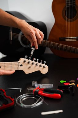Tornavida ve aletlerle Gitar Tamiri. Müzisyen gitar başlığını hassas aletlerle tamir ediyor, ayarlama mandallarını sıkılaştırıyor. Gitar başlığı dikkatlice tornavidayla ayarlanmış.