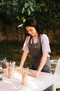 Önlüklü genç bir kadın dışarıdaki çömlek atölyesinde kil serpiştiriyor. Kil, geleneksel çömlekçiliği tanımlayan sanat ve zanaatkarlık için hazırlanıyor.