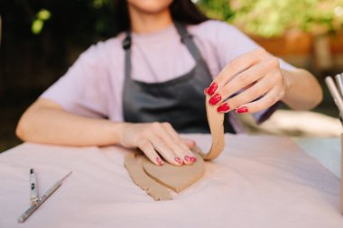 Seramik sanatçısı tasarımları düzenli bir hassasiyetle kil haline getiriyor. Çömlekçilik Clay 'i yakın plan çekiyor. Seramik sanatın ilk aşamalarında şekillendirme aracı kullanılarak kilden kesin kalıplar kesiliyor