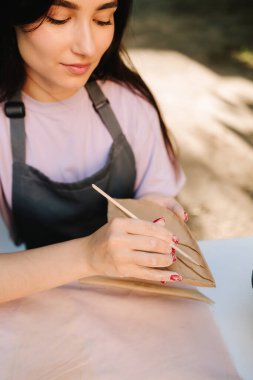 Clay Leaf 'i oyan kadın. Genç bir kadın çömlekçilik yeteneklerini sergilemek için kilin içine ince yaprak desenleri oyuyor. Sanatçı, ayrıntılı çizgileri olan bir kil yaprağını oyuyor
