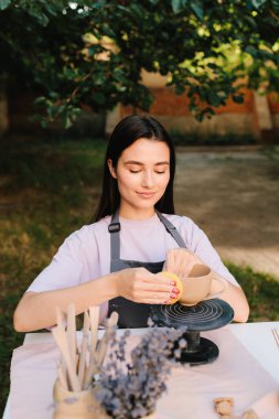 Sanatçı kilden bir kase üzerinde dikkatle çalışır, şeklini süngerle düzeltir. Clay Bowl 'u şekillendiren genç kadın. Potter, tekerleğinde sünger olan, şekil ve dokuyu rafine eden bir kilden kaseyi yumuşatıyor.