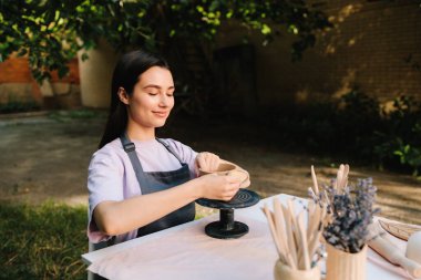 Sanatçı kilden bir kase üzerinde dikkatle çalışır, şeklini süngerle düzeltir. Clay Bowl 'u şekillendiren genç kadın. Potter, tekerleğinde sünger olan, şekil ve dokuyu rafine eden bir kilden kaseyi yumuşatıyor.