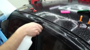 Detaylandırma Merkezi 4k videosunda Islak PPF Uygulaması. Boya koruma filminin ıslak uygulaması hava kabarcıklarını önler ve mükemmel bir uyum için ayarlamaya izin verir.