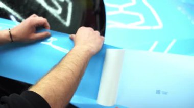 4K videosu tüm detaylarıyla incelenirken arabaya PPF ambalajı uygulanıyor. Detaylandırma merkezine kalın mavi vinil ambalaj kurulumu. Detaylar hatları sığdırmak için ustalıkla paket uygular ve pürüzsüz, pürüzsüz paket hizalamasını sağlar.