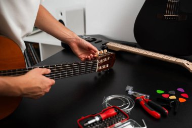 Gitar teli değiştirme ve akort hazırlığı. Müzisyen, aletleri ve yedek telleri kullanarak gitar çalar. Gitar akort süreci raptiyeleri ayarlamayı ve daha iyi ses için yeni dizgiler hazırlamayı içerir