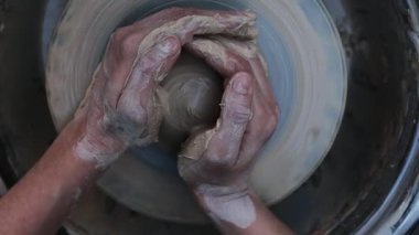Eller tekerlek üzerinde kilin ortasına 4K video çekiyor. Clay şekillenmeden önce dengeyi sağlamak için bir çömlek çarkına odaklanmış. Çamur dönen bir çömlek çarkında şekillenir, seramik bir kabın ilk formunu yaratır..