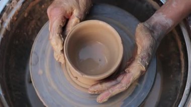 Potter, 4K 'lık bir videoda killi kase şekillendiriyor. Çamur, çömlekçi çanağı oluştururken el altında yavaşça döner. Tekerlekteki kil kalıpları çömlek sanatını ve yeteneğini ön plana çıkarıyor.