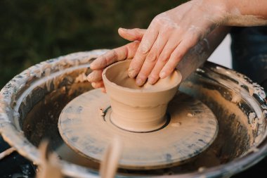 Potter tekerlek üzerinde kil kaseyi şekillendiriyor. Çamur, çömlekçi çanağı oluştururken el altında yavaşça döner. Tekerlekteki kil kalıpları çömlek sanatını ve yeteneğini ön plana çıkarıyor