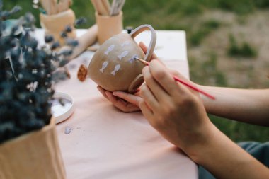 Fırça darbeleriyle balık desenli kupa seramik resmi. Sanatçı el yapımı kil bardağa narin mor balıklar çiziyor. Fırça ve boya kullanarak mor balıkla seramik bardak boyama