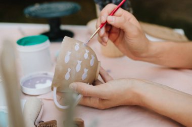Fırça ve boya kullanarak seramik bardağı mor balıkla boyamak. Fırça darbeleriyle balık desenli kupa seramik resmi. Sanatçı, el yapımı kil bardağa narin mor balıklar çiziyor.