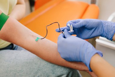 Steril eldiven giyen hemşire venipunktur yaparak kontrollü bir klinik ortamda tanı testi için kan topluyor. Kan koleksiyonu için bir iğne yerleştir.