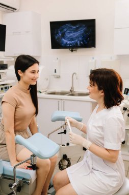 Jinekolog, muayene sırasında teşhis aletini gösteriyor. Jinekolog muayeneden önce aletlerin kullanımını tartışır. Doktor jinekolojik muayene için tıbbi aletler hazırlıyor.