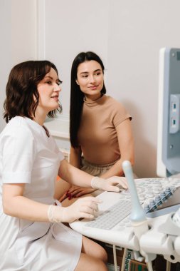 Jinekolog ve kadın muayene sırasında ultrason görüntülerini tartışıyor. Jinekoloğa danışıyorum. Jinekolog ve hasta ultrason taramasının sonuçları ekranda birlikte görünüyor.