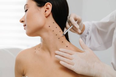 Nefertiti boynundaki işaretli noktalarla enjeksiyonu kaldırıyor. Kozmetik uzmanı kızın platizmasına botulinyum toksini enjekte edilmeden önce nokta çiziyor.