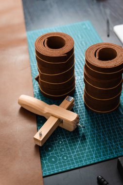 Sharp strap cutter and leather rolls, essential for crafting accurate belt straps. Leather rolls and strap cutter lie on cutting mat, ready for trimming strong belts and leather goods