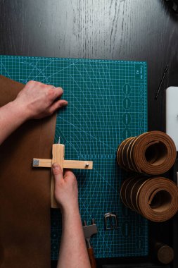 Zanaatkar, hasırın üzerinde tahta kesici kullanarak deri kayış hazırlıyor. El yapımı deri kemer hazırlığı, hasırın üzerinde tahta kayış kesici var. Esnaf deri şeritleri tahta aletlerle kesiyor.