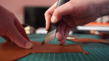 Zanaatkar deriyi dikkatli bir şekilde kesiyor. 4K video. Zanaatkar, deri parçaları titizlikle keserek, doğru şablonları sağlayarak hazırlar. Bıçakla deri keser.