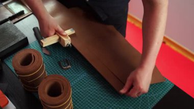 Zanaatkar 4K videosunda ahşap kesici kullanarak deri kayış hazırlıyor. El yapımı deri kemer hazırlığı, hasırın üzerinde tahta kayış kesici var. Esnaf deri şeritleri tahta aletlerle kesiyor..