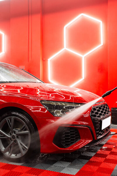 High pressure car rinse removes dirt, foam, and road grime from body panels and headlights of red sports car. Paint safe car rinse with high pressure water removes debris, soap residue, and dirt