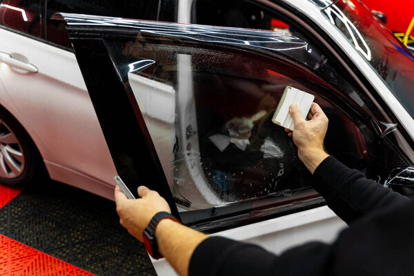 Detailer apply dark tint film to car side windows using a squeegee for smooth, bubble-free adhesion. Smoothing dark tint film on side windows removes air bubbles and ensures perfect alignment