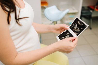 Hamile bir kadın karnındaki bebek ultrasonu fotoğrafına bakar. Anneliğin değerli anlarını ultrasonla filme alıyorum.