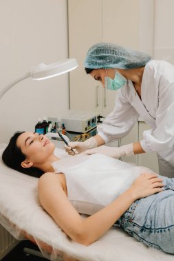 Cildiyeciler radyoaktif gerilim ameliyatı kullanarak kesin bir radyo dalgası temizliği yapıyorlar. Radyo dalgası dermatolojik mol kesimine yakın çekim. Klinik koşullar altında radyoaktivite köstebeği temizleme