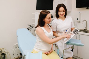 Jinekolog doktor, check-up sırasında bebek bekleyen hastalara danışmanlık yapıyor. Hamile kadın klinikte jinekoloğuyla konuşuyor.